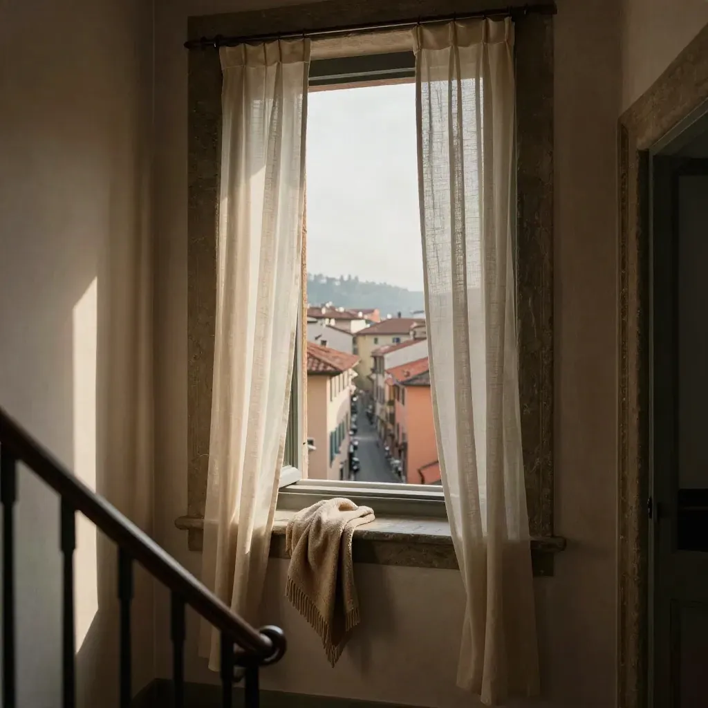 Interno fiorentino con finestra, tende chiare e tetti rossi lontani, visto da un pianerottolo.